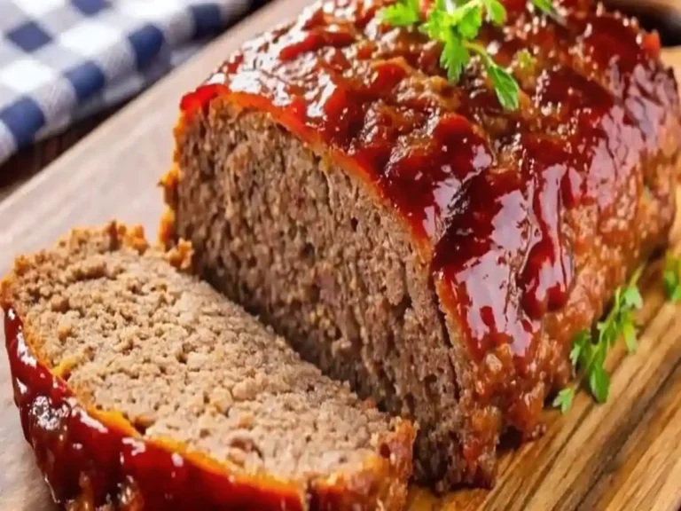 Close-up of a glazed meatloaf topped with parsley, served on a wooden board with one slice cut.
