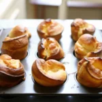 Freshly baked popovers with crispy edges in a muffin tin, showing their unique puffed shapes.