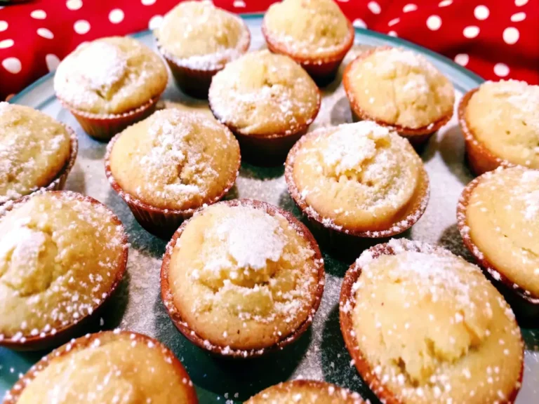 A plate of mini lemon cakes dusted with powdered sugar, arranged against a red polka-dot fabric background for a festive and vintage aesthetic.