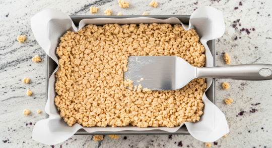 Pressing Rice Krispie mixture into a parchment-lined pan