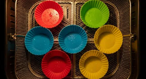 Oiled silicone cups preheating in an air fryer basket for stuffing muffins