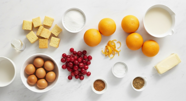Cranberry Orange Bread Pudding ingredients flat lay with brioche, cranberries, oranges, eggs, milk