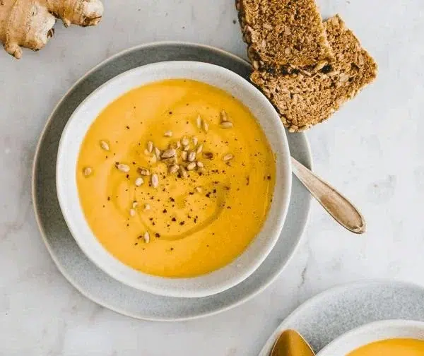 Bowl of vegan carrot ginger soup topped with fresh herbs.