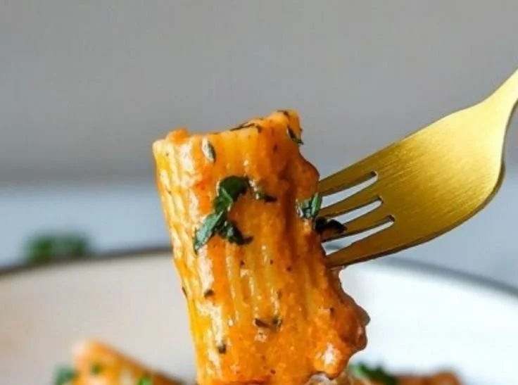 A bowl of creamy tomato garlic rigatoni pasta garnished with fresh herbs