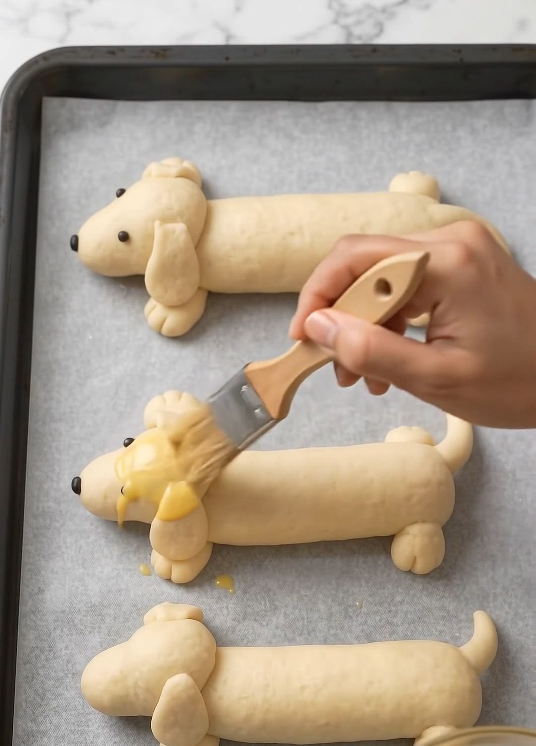 Brushing dachshund-shaped rolls with egg wash before baking